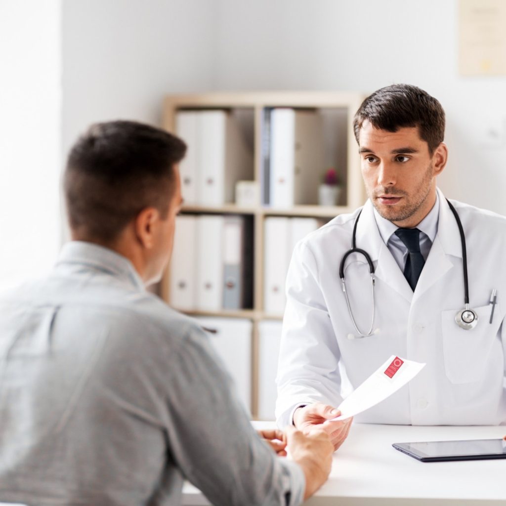 Doctor in white coat handing patient in grey shirt a referral to Imaging Queensland