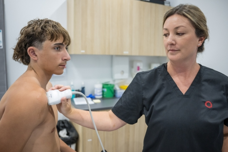 Sonographer does ultrasound of young male patient's shoulder.