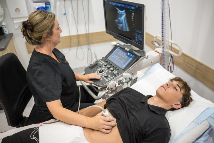 Sonographer scans abdomen of young male patient.