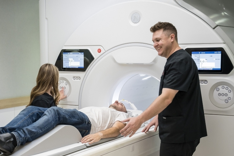 Two MRI Technologists support patient as he goes into MRI scanner.